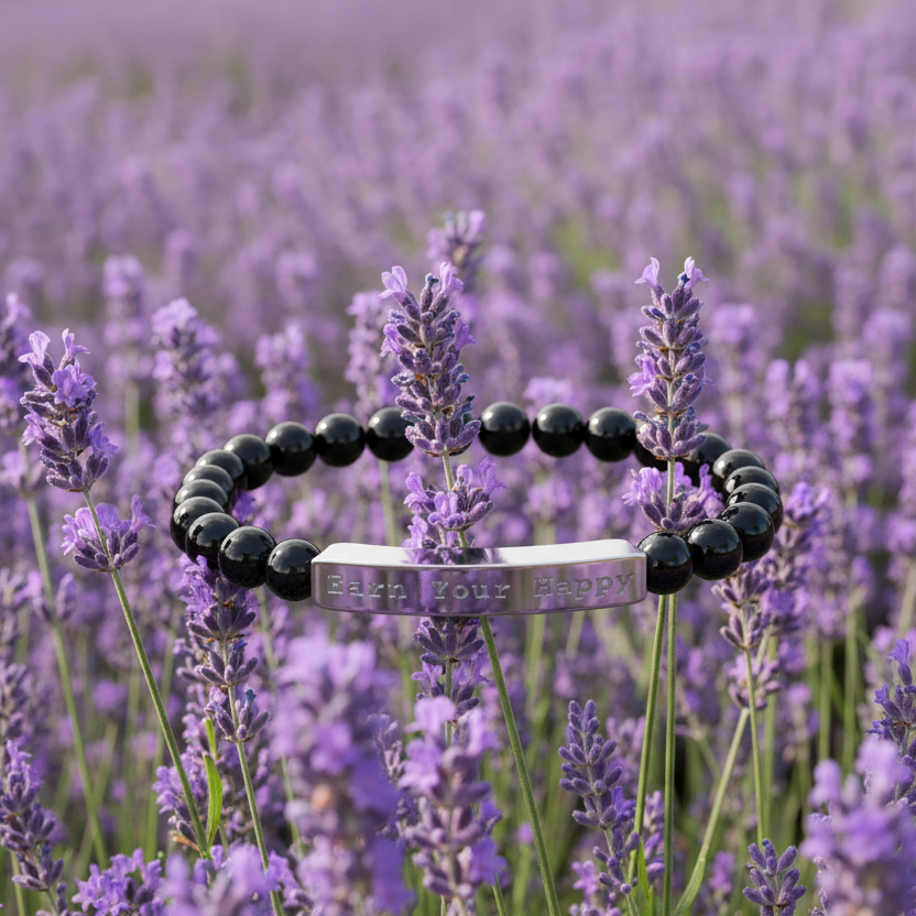 Natural Stone black beaded stretch bracelet with a silver engraved "Earn Your Happy" in a field of lavender background