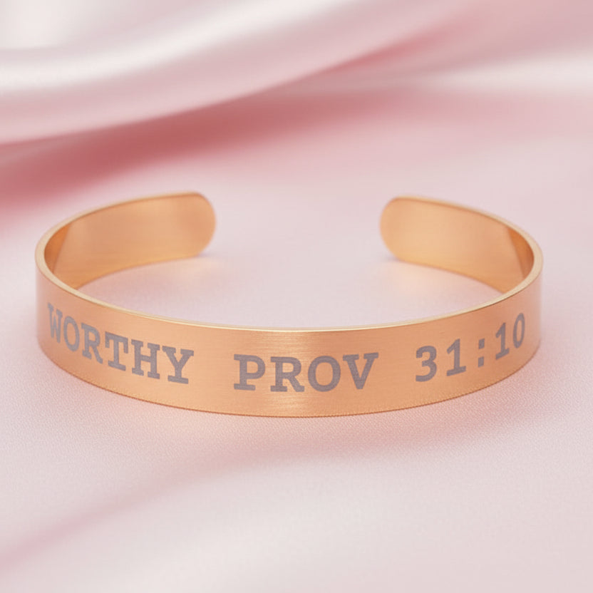 Gold bracelet with 'Worthy Prov 31:10' engraving on a pink fabric background