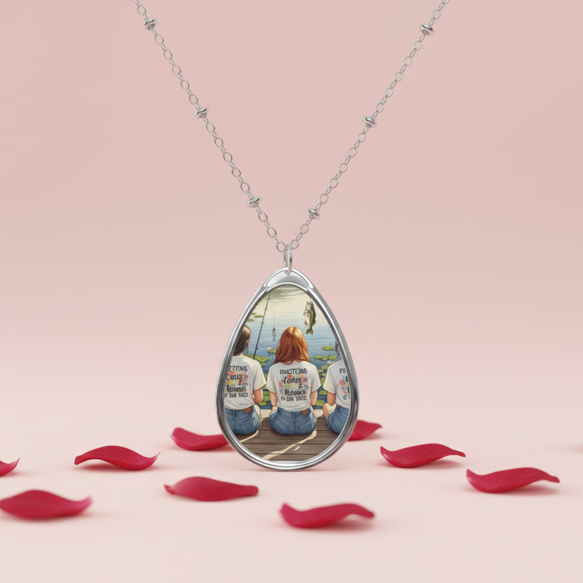 Teardrop-shaped necklace with a pendant featuring a person in a park, surrounded by red petals on a pink background.