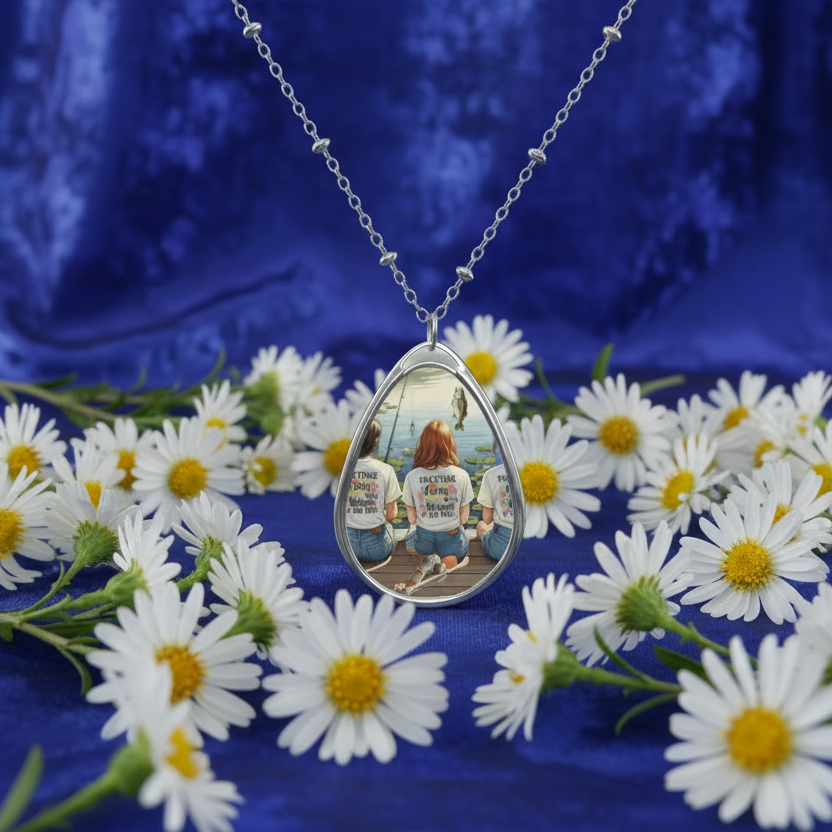 Teardrop-shaped necklace with a photo pendant on a blue fabric background with white flowers.