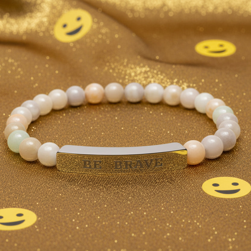 Natural stone bracelet with 'BE BRAVE' tag on a gold fabric background with smiley faces
