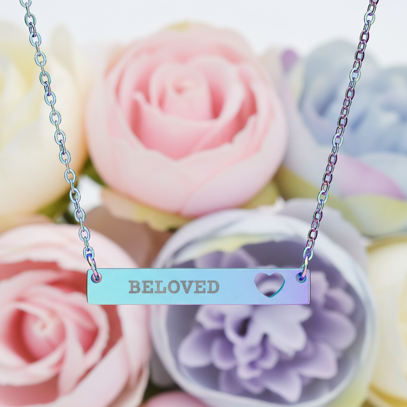 Necklace with 'Beeloved' pendant in front of colorful flowers
