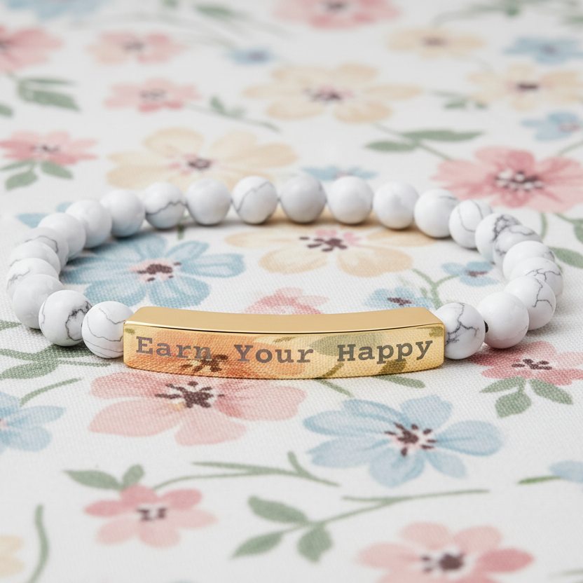 Natural Stone stretch beaded bracelet with a gold bar "Earn Your Happy" on a floral fabric background
