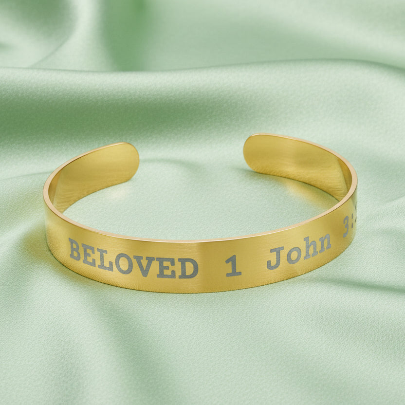 Gold cuff bracelet with engraved text on a green fabric background
