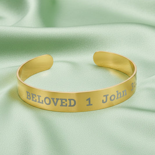 Gold cuff bracelet with engraved text on a green fabric background