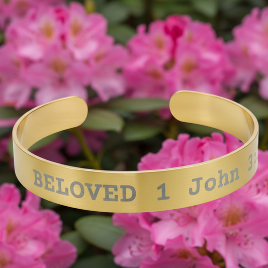 Gold bracelet with 'Beloved 1 John 3' engraving on a pink floral background

