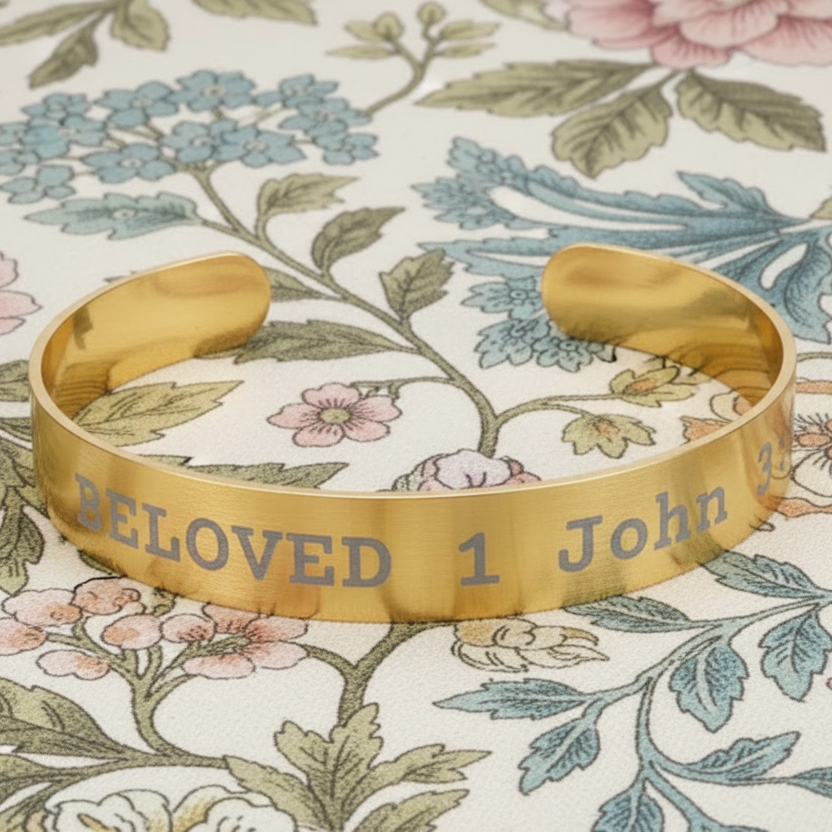 Gold cuff bracelet with 'Beloved 1 John' engraving on a floral background