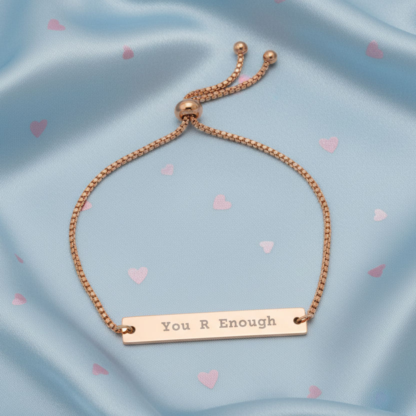 Rose gold bracelet with 'You R Enough' bar on a blue background with heart shapes