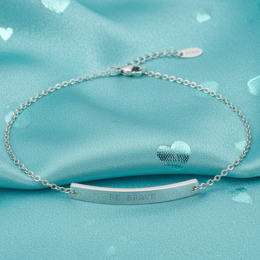 Silver anklet with 'BE BRAVE' engraving on a turquoise fabric background