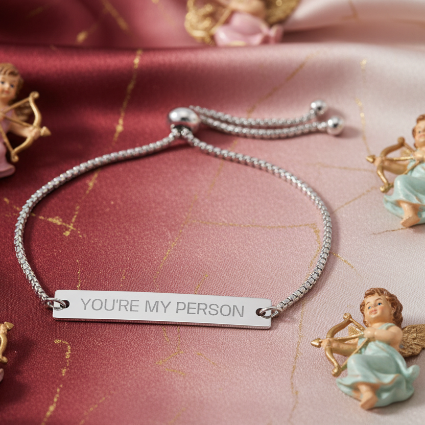 Silver bracelet with 'YOU'RE MY PERSON' tag on a decorative background with angel figurines.
