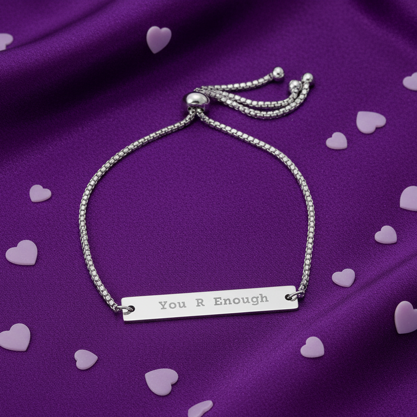 Silver bracelet with 'You R Enough' tag on a purple fabric background with heart shapes