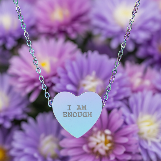 Necklace with a heart-shaped pendant reading 'I AM ENOUGH' against a background of purple flowers.