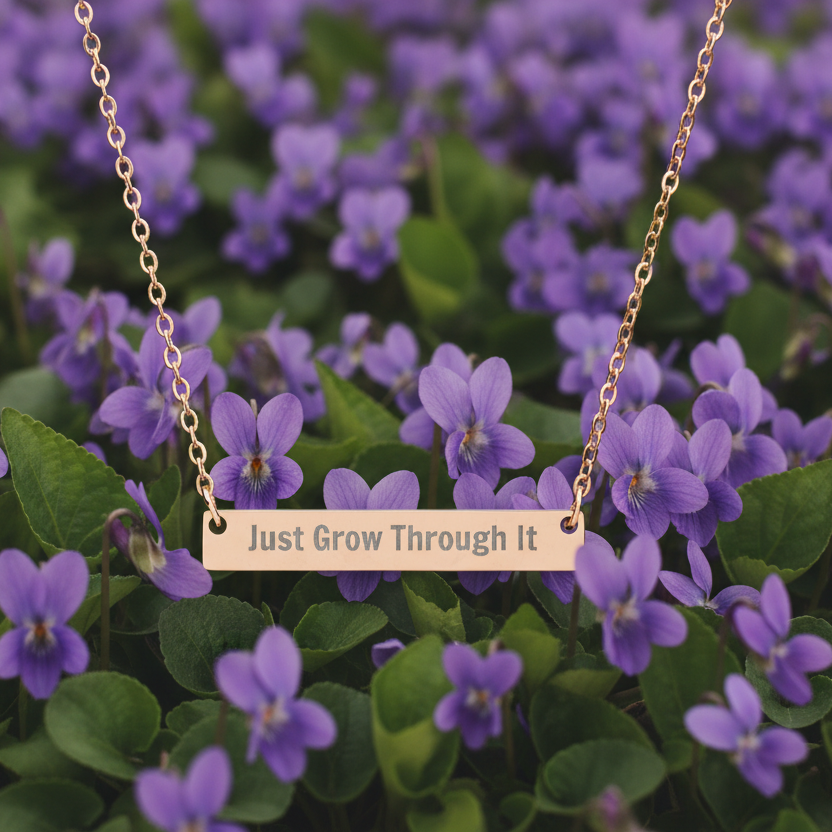 Necklace with 'Just Grow Through It' pendant on a background of purple flowers