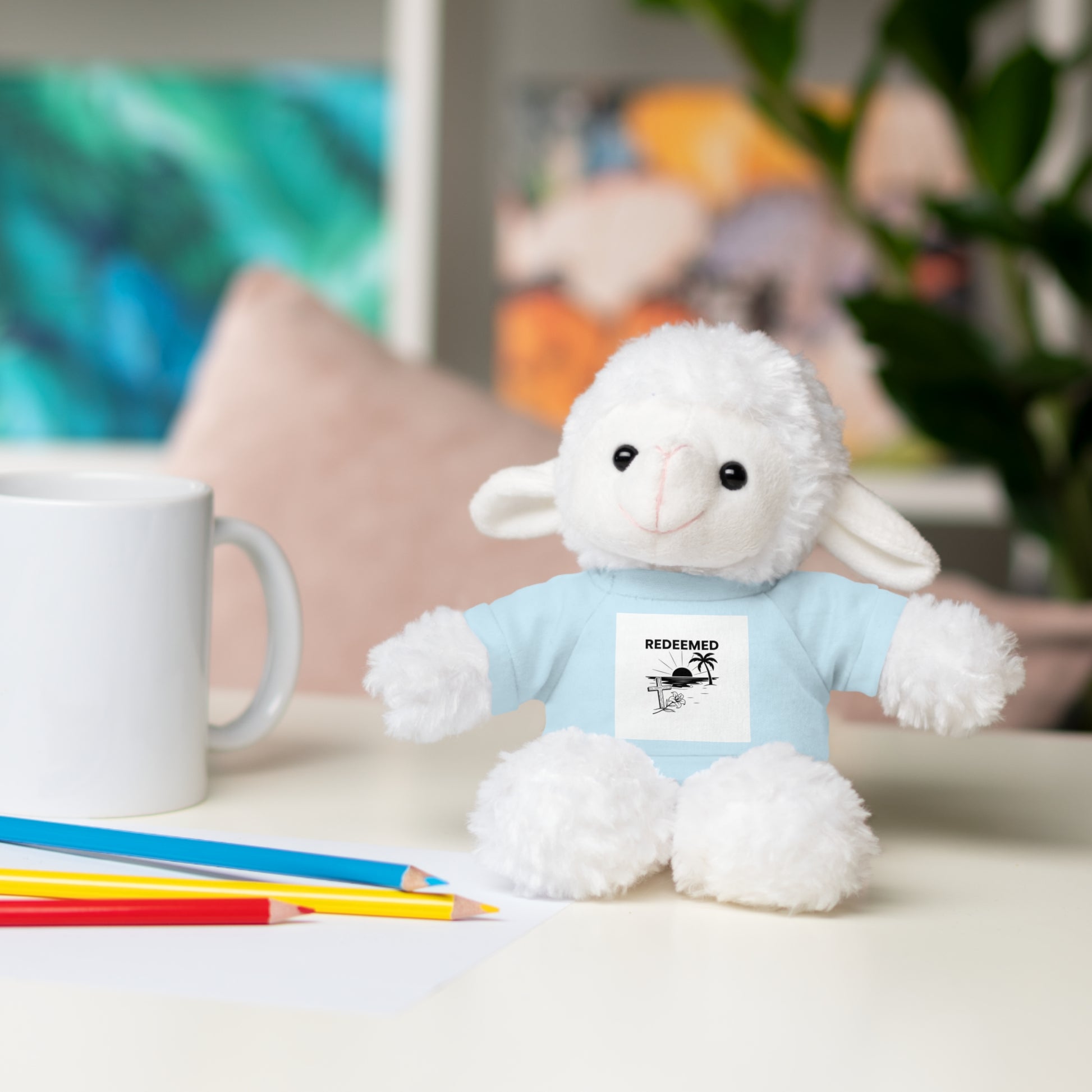 White plush lamb toy with a blue shirt on a table with a mug and pencils.