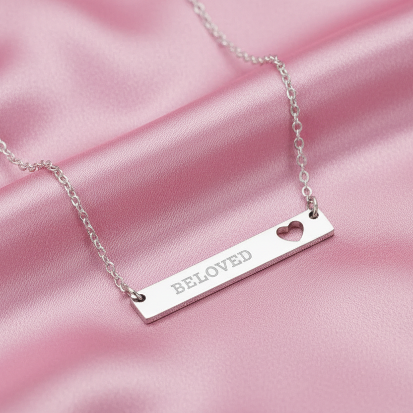 Silver necklace with 'Beloved' pendant on a pink satin background