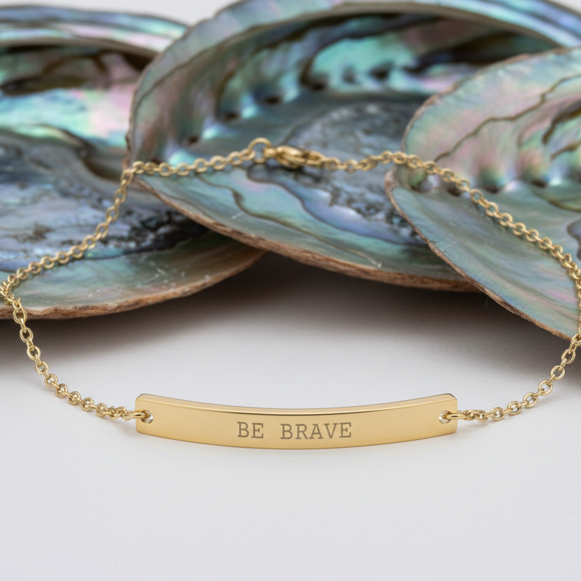 Gold anklet with 'BE BRAVE' engraving on a white background