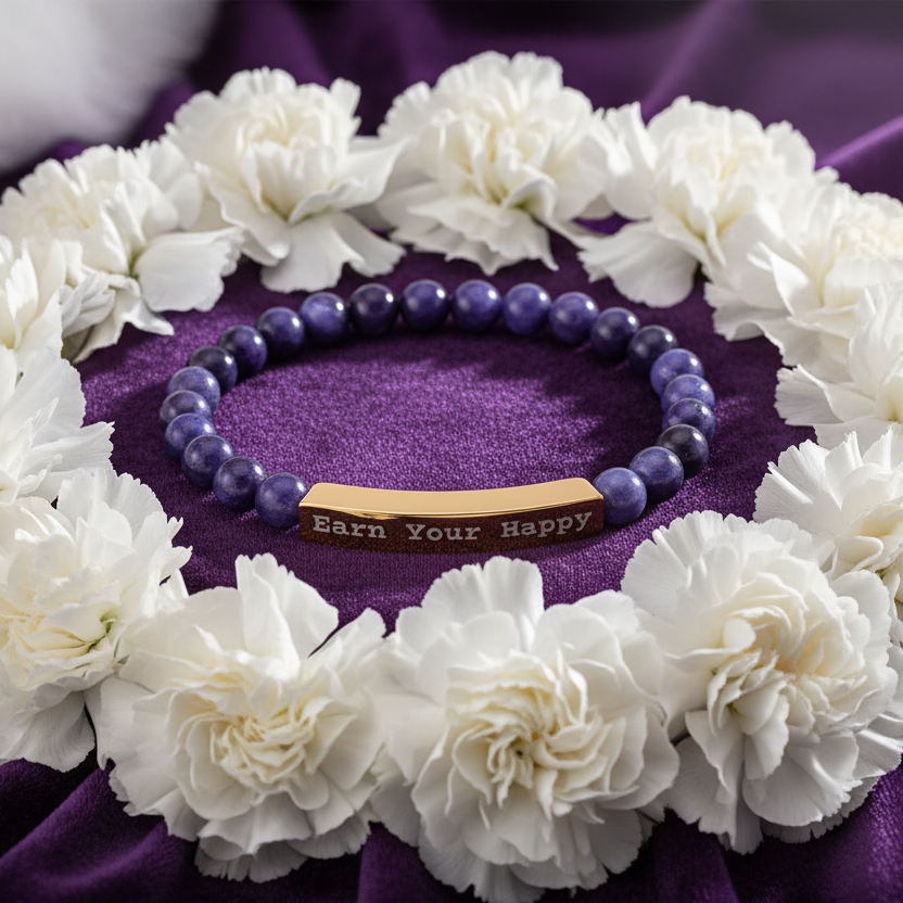Natural Stone stretch beaded bracelet with a gold engraved "Earn Your Happy" on a purple fabric surrounded by white flowers