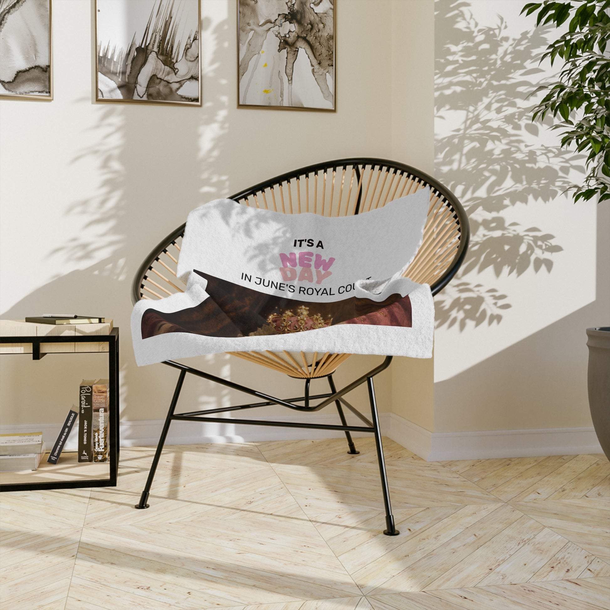 Queen June in regal attire with a crown and text 'It's a New Day in June's Royal Court' on a white background velvet lap throw on a chair in a sunlit room.