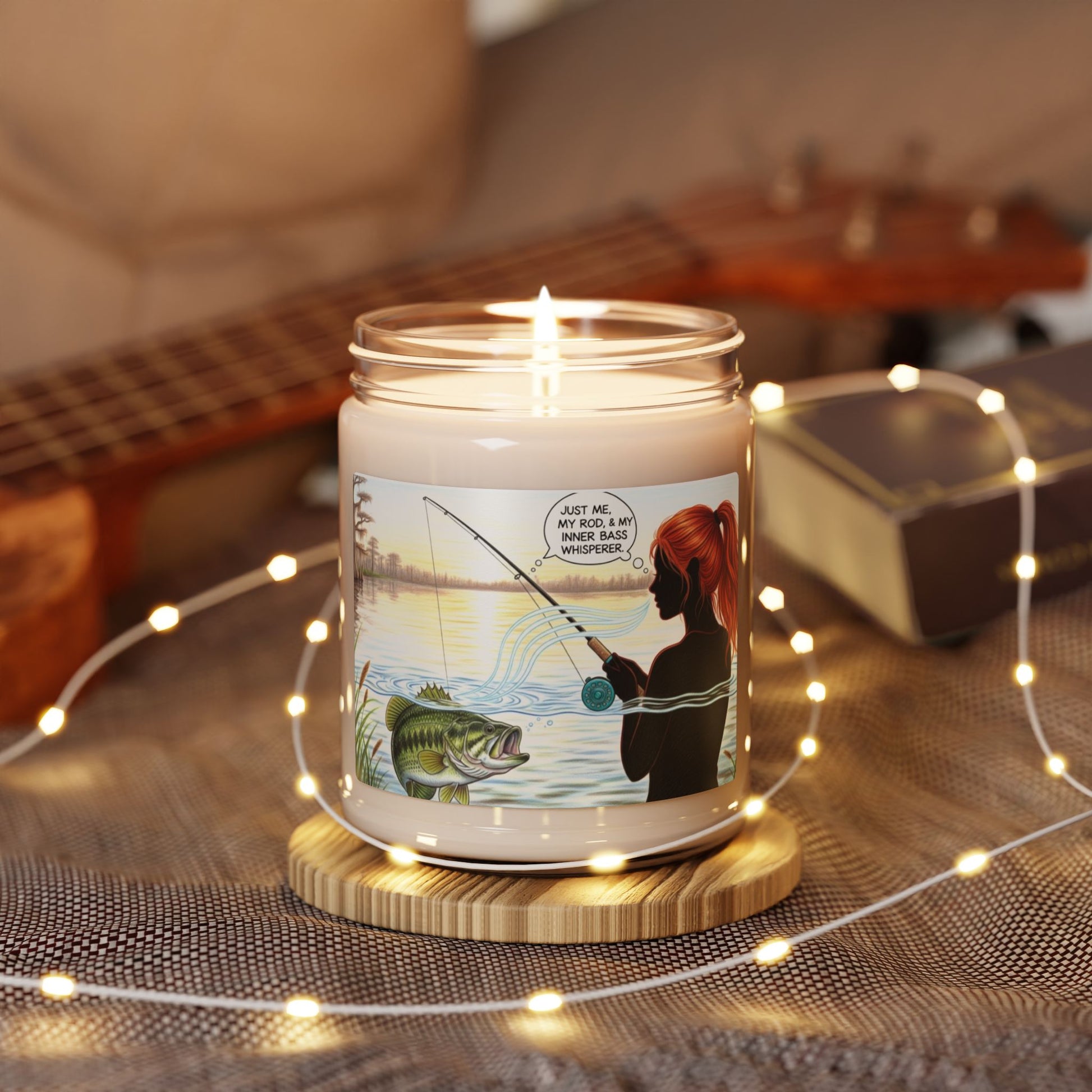Candle with a fishing design on a wooden coaster surrounded by string lights, with a guitar in the background.