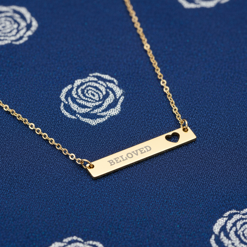 Gold necklace with 'BELoved' pendant on a blue fabric background with floral patterns