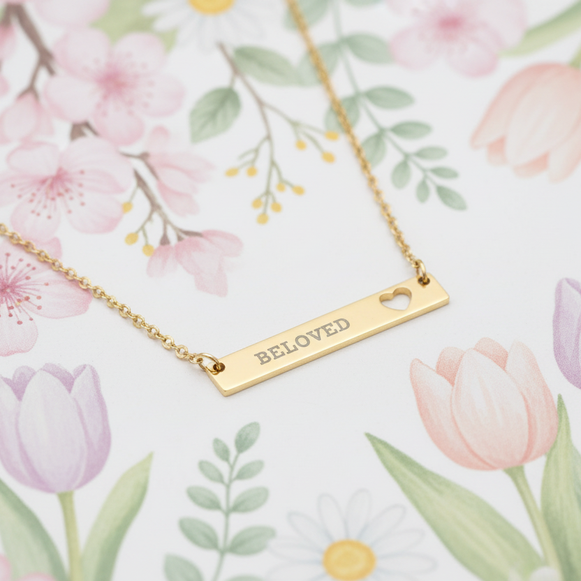 Gold necklace with 'BELOVED' pendant on a floral background