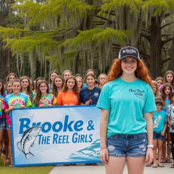 Woman in a blue shirt and shorts standing in front of a group of people with 'Brooke & The Reel Girls' sign.